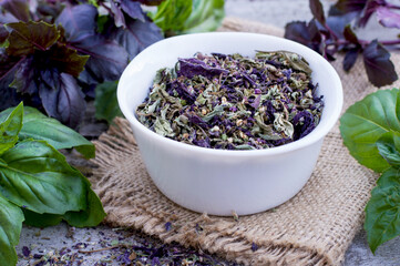 Dried basil in a bowl and fresh basil leaves on a wooden background. Green and purple basil..