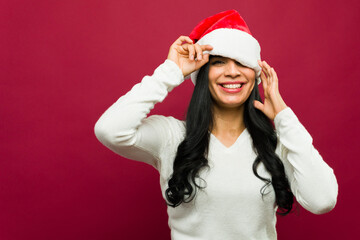 Studio portrait of a young woman adjusting her santa claus hat over her eyes and smiling on a red background