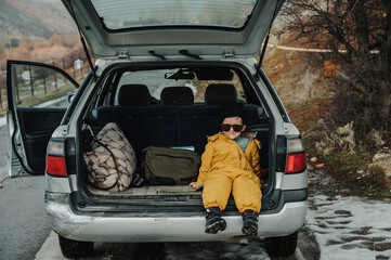 A boy enjoys the view while sitting in the open trunk of a car.