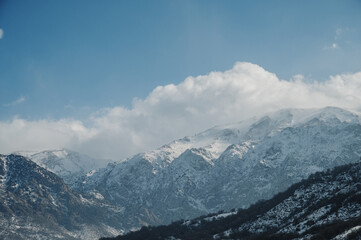 Panoramic view of snow-capped mountains against a blue cloudy sky.