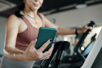 Fototapeta premium Woman using smartphone while running on treadmill in gym