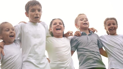 Obraz premium a group of children jumping in the park on the grass embracing. happy family childhood dream concept. little kids jump hugging each other by the shoulders. children smiling and laughing lifestyle