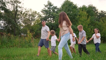 Fototapeta premium family walking on the grass in the park and holding hands. happy family childhood dream concept. a large family walks across the clearing and talks to each lifestyle other. outdoor nature walk