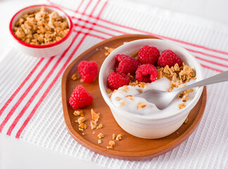 Raw plain non-dairy yogurt made from coconut topped with raspberries and granola with a spoon; plant-based diet; copy space