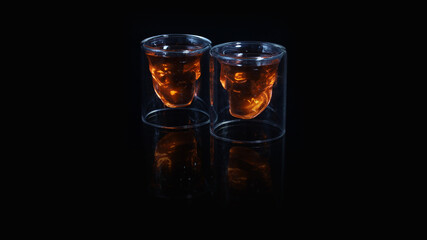A pair of skull shaped shot glass filled with a red orange drink on a black background