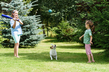 Fototapeta premium Girls playing with baseball bat in garden and dog catching ball