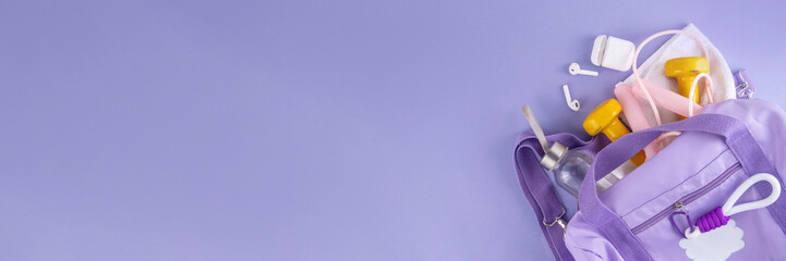 Sport and fitness background. Women's sports bag with dumbbells, bottle of water, towel, jump rope, headphones, accessories for sports and fitness on light purple background, copy space