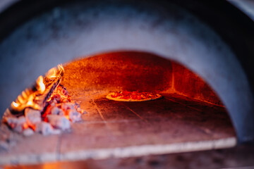 Valmiera, Latvia - August 17, 2024 - Summer festival. A pizza bakes inside a wood-fired oven with glowing embers, creating a warm and rustic atmosphere. The pizza is partially cooked.
