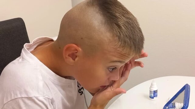 an 11-year-old boy puts on night lenses while sitting at a table in front of a mirror, contact, orthokeratological, night