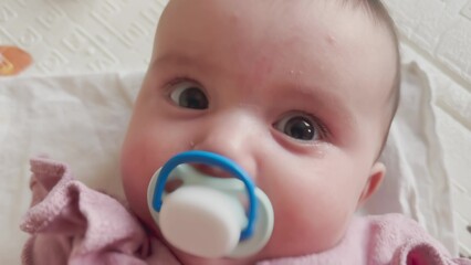 baby girl with pacifier. a kindergarten happy family kid dream concept. newborn 6 months close-up sucking rubber pacifier looking at camera lifestyle