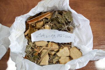 Asian traditional herbs and spices, dried and prepared, shown on a wooden table, on tissue or in cups.