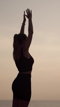 Young beautiful woman practicing yoga on ocean beach in morning, vertical video. Sport workout for stay slender and healthy, sportive lifestyle, body care and breathing exercise, relax and meditation