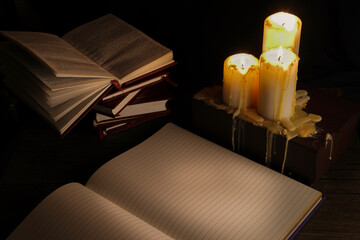 Three candles burning dancing flame light on book copy pen turning pages black background