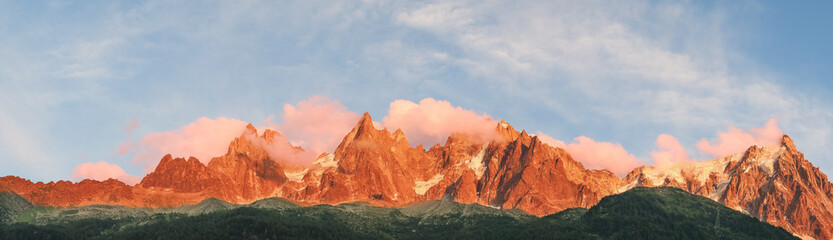 Naklejka premium Dramatic Panoramic Landscape Of Snow Capped Mountain Peaks Glowing In Warm Sunset Light With Pink Clouds