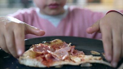 Child carefully examining and holding a pizza slice with both hands before taking a bite, illustrating the curiosity and engagement of a young boy during a meal