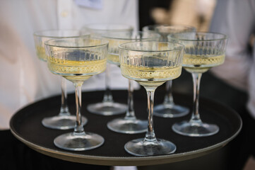 Tray of glasses of summer sparkling wine for guests at wedding reception. The waiter serving champagne on tray. Waiter holding glasses in backyard. Woman brings full glasses of champagne closeup.