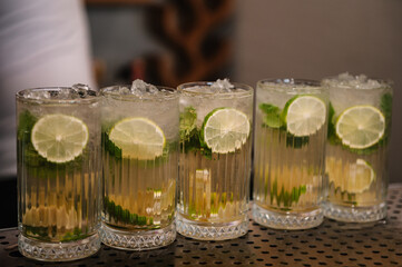 Closeup of bartender preparing Mojito cocktail on a bar counter. Waiter with a mojito cocktail. Unrecognizable bartender holding mojito cocktail with mint leaves, and lime in restaurant.