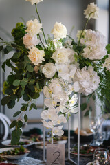 Table number 2. Stands, sign number two. Setup detail. Luxury reception. Elegant table decorated composition flowers in party area. Beautifully organized event. Wedding hall with atmospheric decor.