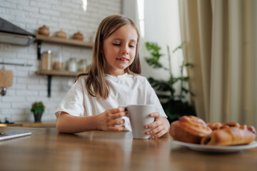 Preteen child holding cup near blurred pastry in kitchen