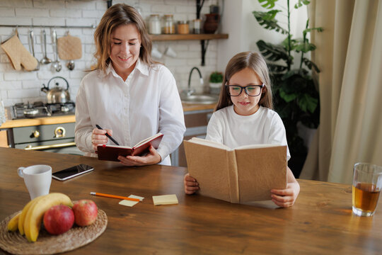 Child reading book near smiling mother working at home