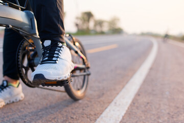 Fototapeta premium Closeup foot of a woman wearing white sneakers stepping on the pedal, going to start riding a bicycle on the asphalt road in countryside