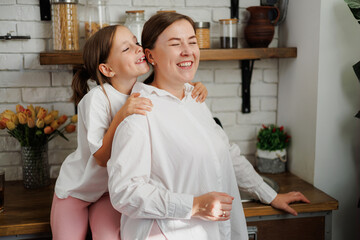 Smiling child hugging mother in kitchen at home