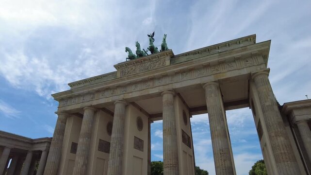Perspective view from below the Brandenburg Gate. Horses atop the gate stand out against a blue sky and suggestive clouds. slight movement to the right 