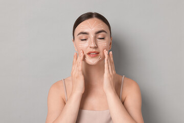 Beautiful young woman doing face massage with fingers on grey background. Lines on skin showing directions of motion