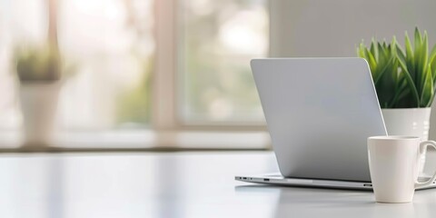 Fototapeta premium laptop and coffee cup on white table in bright office, blurred background of modern home interior with window.