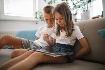 Obraz premium Two children sit on a sofa, engrossed in a tablet computer
