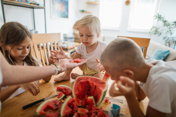 Mother serves her kids fresh watermelon at the table