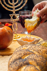 Women's hands dip challah in honey at a table with traditional Rosh Hashanah wine and pomegranate