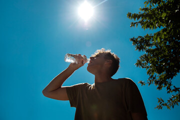 Young handsome man drinking water in hot sunny day. Surviving the heat concept
