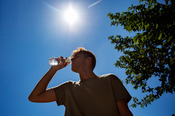Young attractive man drinking cold water in sunny day. Surviving the heat concept