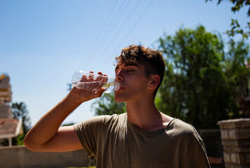 Young attractive man drinking cold water in sunny day. Surviving the heat concept