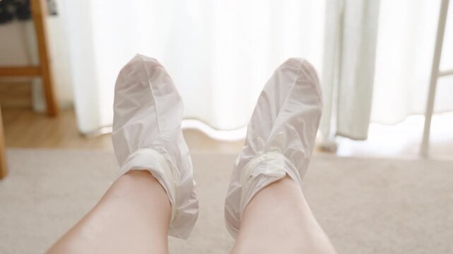 A Close-up of a Woman feet raised slightly, wrapped in white socks for a foot peeling treatment, highlighting the skincare process.
