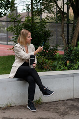 Woman sitting outdoors using smartphone and drinking coffee.