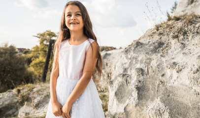 Beautiful cheerful little girl in white dress on a nature background. Smiling child otside.