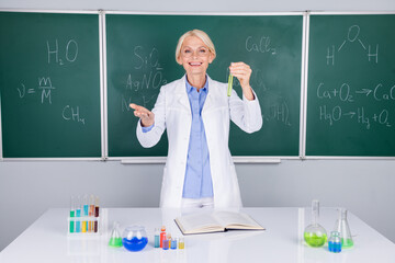 Photo of positive pretty intelligent senior lady wear white coat doing chemical research isolated on green board background