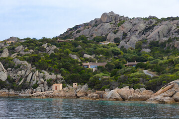 Una vista de la costa de Punta Cerde&ntilde;a, Italia, muestra un paisaje escarpado con grandes formaciones rocosas de granito que se mezclan con la densa vegetaci&oacute;n mediterr&aacute;nea.