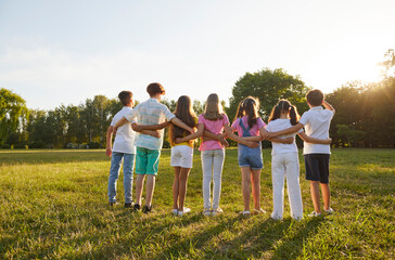 Kids huddling in the park in summer. Friends playing together in nature. From behind group children...