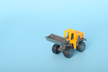 The image portrays a yellow toy backhoe loader with a raised bucket, set against a vibrant blue...