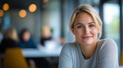 A confident businesswoman with blonde hair smiles while seated at a stylish office table, surrounded by a collaborative environment. copy space.