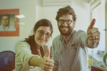 Obraz premium Two smiling colleagues in an office give a thumbs-up, reflecting positivity and teamwork.