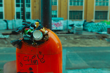 An overfilled trash can with a lot of garbage sticking out of the opening, city cleanliness, urban overfilled trash can