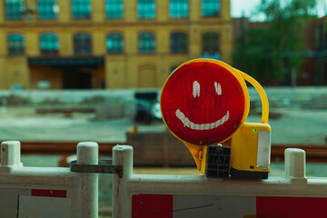 A construction site lamp on which a laughing face has been painted, construction site barrier with a warning lamp in red where a laughing face has been painted

