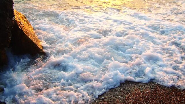 Waves gently lap at shore during stunning sunset over ocean. Golden sunlight reflects off waves as they roll onto shore, creating tranquil atmosphere at sunset by sea. Montenegro summer Canj