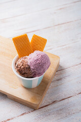 Two ice cream scoops on ceramic cup with 2 wafers. above angle. Wooden board and rustic table