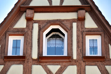 Traditional half-timbered house facade, showcasing three windows with lace curtains, framed by wooden beams. Nurember, Baviera.