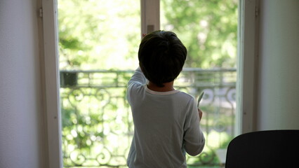 Young boy reaching for the window knob, stepping out onto the balcony to explore, and returning home to close the window. curiosity and interaction with the outdoor environment